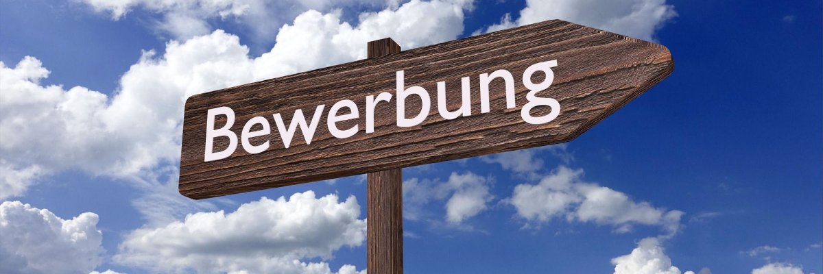 Holzschild als Wegweiser Ein Wegweiser aus Holz mit der Aufschrift "Bewerbung", Im Hintergrund ist blauer Himmel mit ein paar dünnen Wölkchen zu sehen.