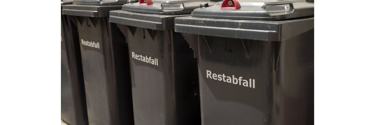 Restabfallbehälter Vier schwarze Restabfallbehälter mit rotem Schloss stehen aneinander gereiht vor einer Hauswand. Sie tragen die Aufschrift Restabfall auf dem Korpus.