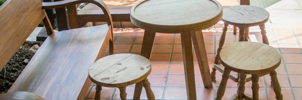 Sitzgruppe gut erhaltene Möbel wie Barhocker, Tisch und Stühle stehen kreisförmig angeordnet auf mit Platten befestigtem Untergrund. Im Hintergrund ist ein Garten mit Teich zu erkennen.