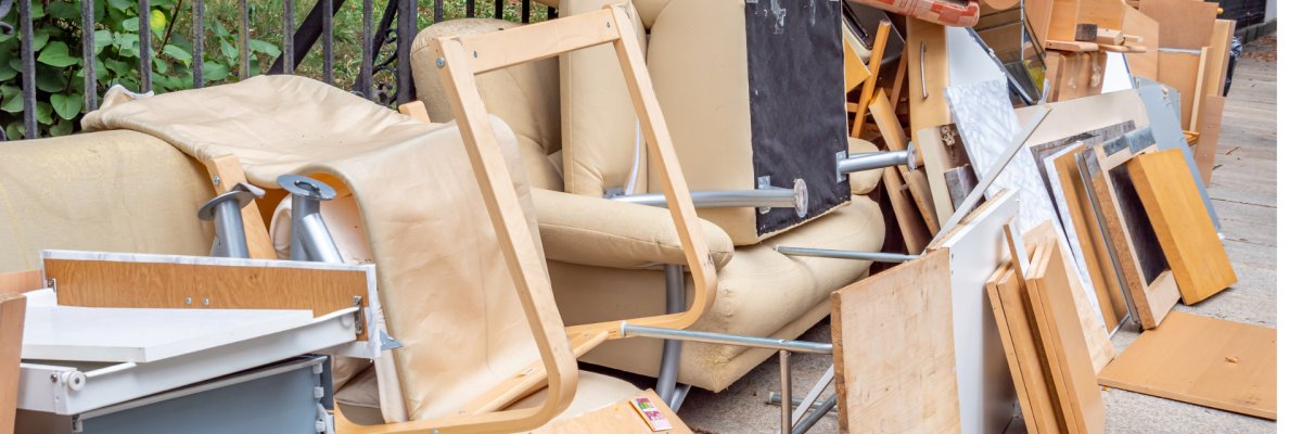 Sperrabfälle in Form von Brettern, Sofaelementen und Schubladen. Diese stehen auf dem Bürgersteig zur Sperrabholung bereit. Im Hintergrund ein Zaun als Einfriedung zu einem Wohngrundstück. 