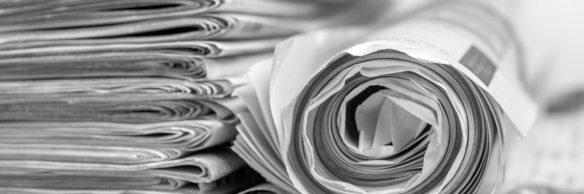 Zeitungsstapel 15 aufeinander gestapelte Zeitungen in schwarz-weis auf grauem Hintergrund. Links daneben eine gerollte Zeitung.
