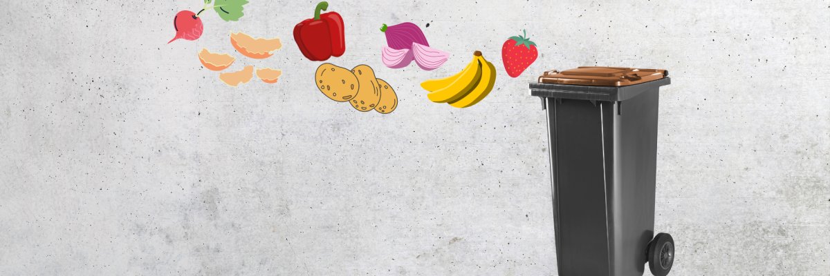 schwarzer Biobehälter mit braunen Deckel. Im Vordergrund frisches Obst und Gemüse, welches optisch in den Abfallbehälter fliegt. 